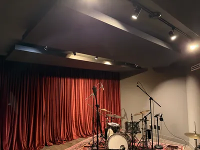 Ceiling clouds and configurable track lighting above the drum kit, curtains drawn