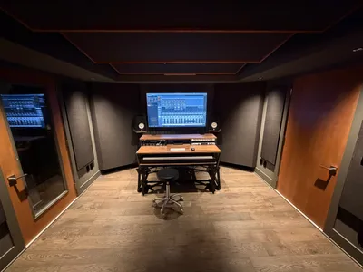 Control room. Yamaha monitors, Apollo interface, and doubled, sealed door to the live room. Clouds overhead, bass traps and absorbers on the walls. Exit to the right.