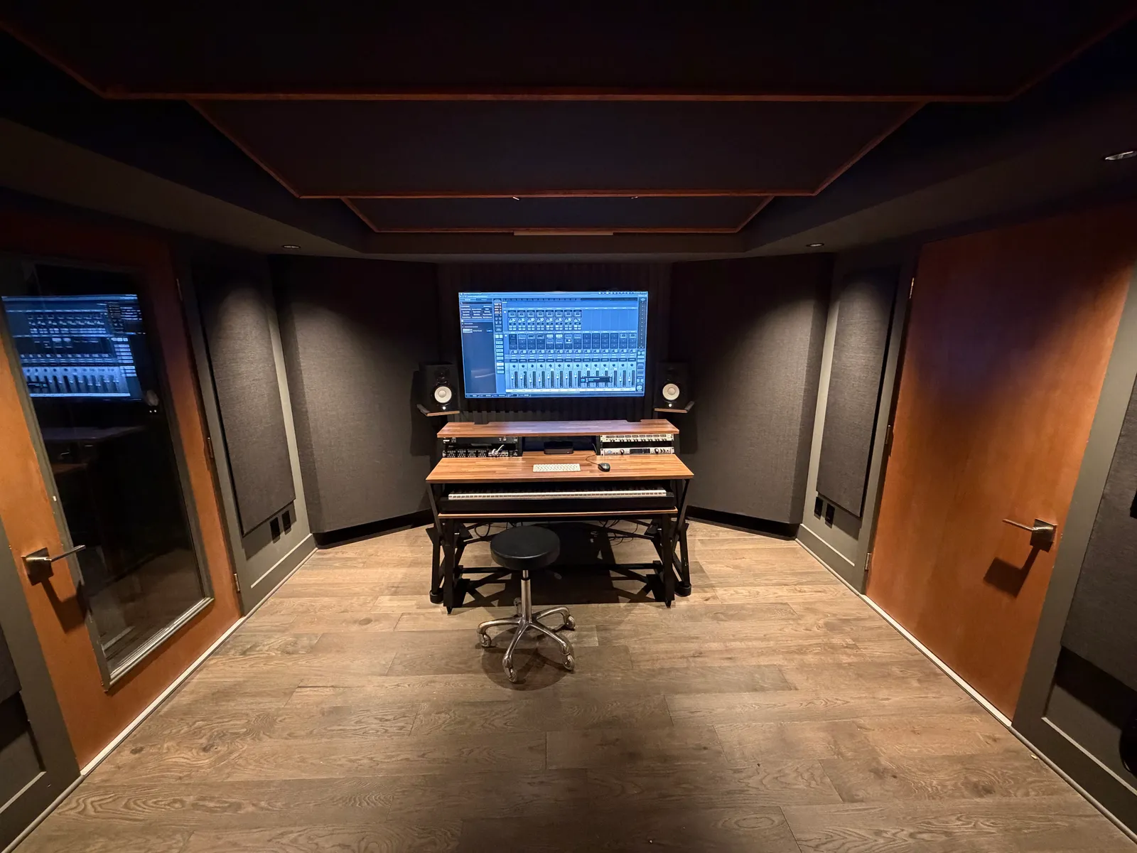 Control room. Yamaha monitors, Apollo interface, and doubled, sealed door to the live room. Clouds overhead, bass traps and absorbers on the walls. Exit to the right.