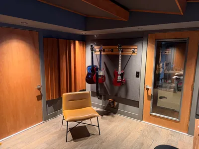 Guitars on the wall, wood diffusers, and a lounge chair in the control room. Doubled, sealed, windowed doors to live room.