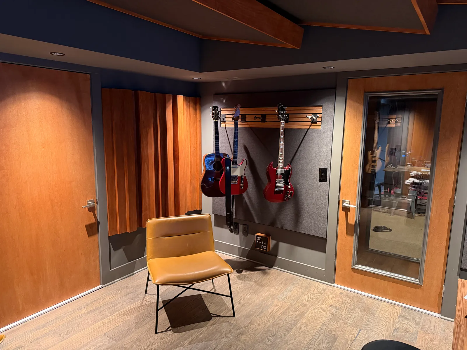 Guitars on the wall, wood diffusers, and a lounge chair in the control room. Doubled, sealed, windowed doors to live room.