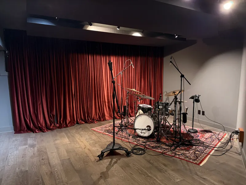 The live room — drum kit set up on a Persian rug, retractable curtains drawn behind