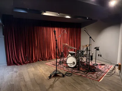 Live room with the drum kit set up, curtains drawn behind, clouds overhead. Tie line panel on the right wall.