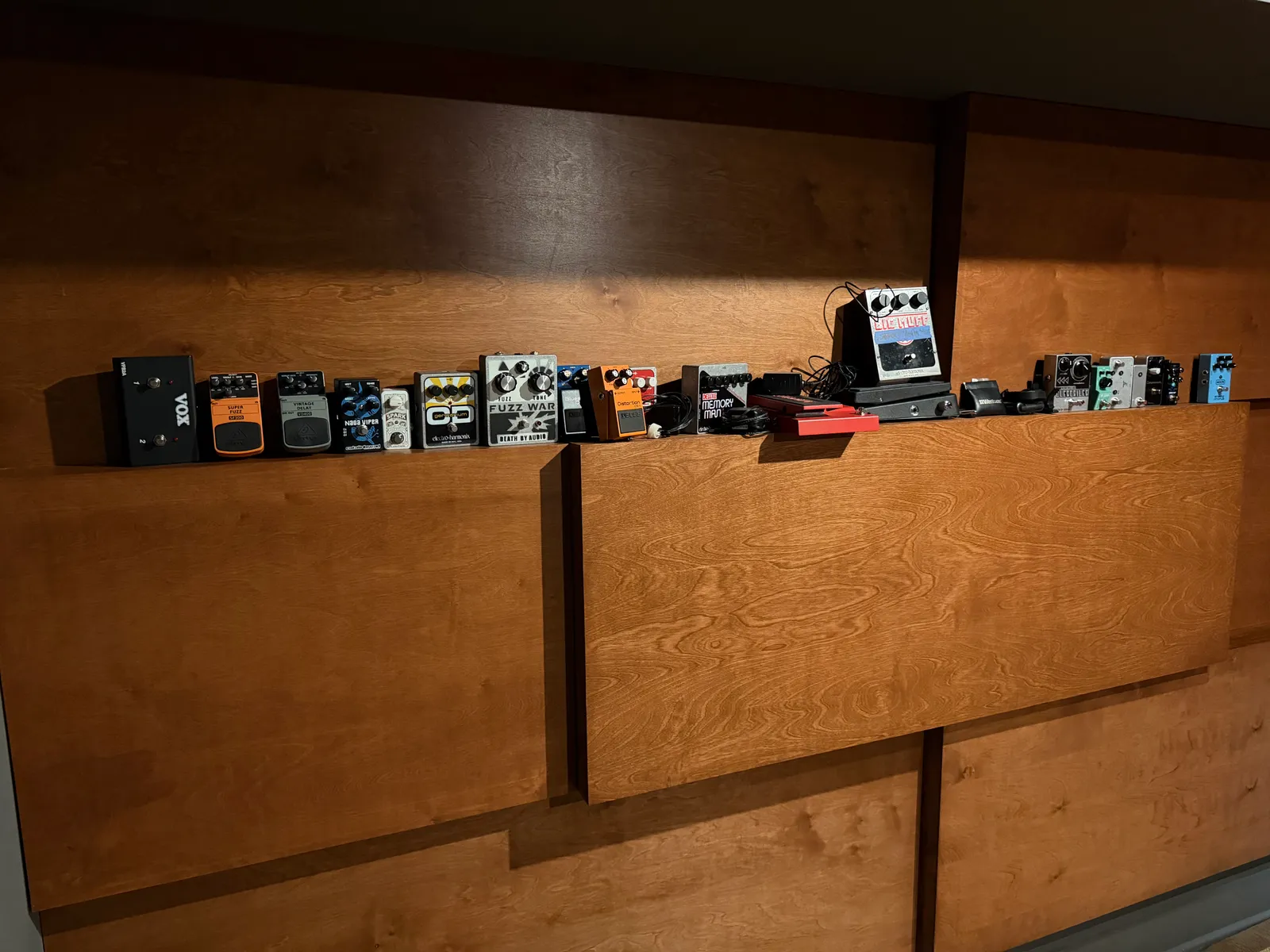 Pedal collection lined up along the wood paneling in the live room